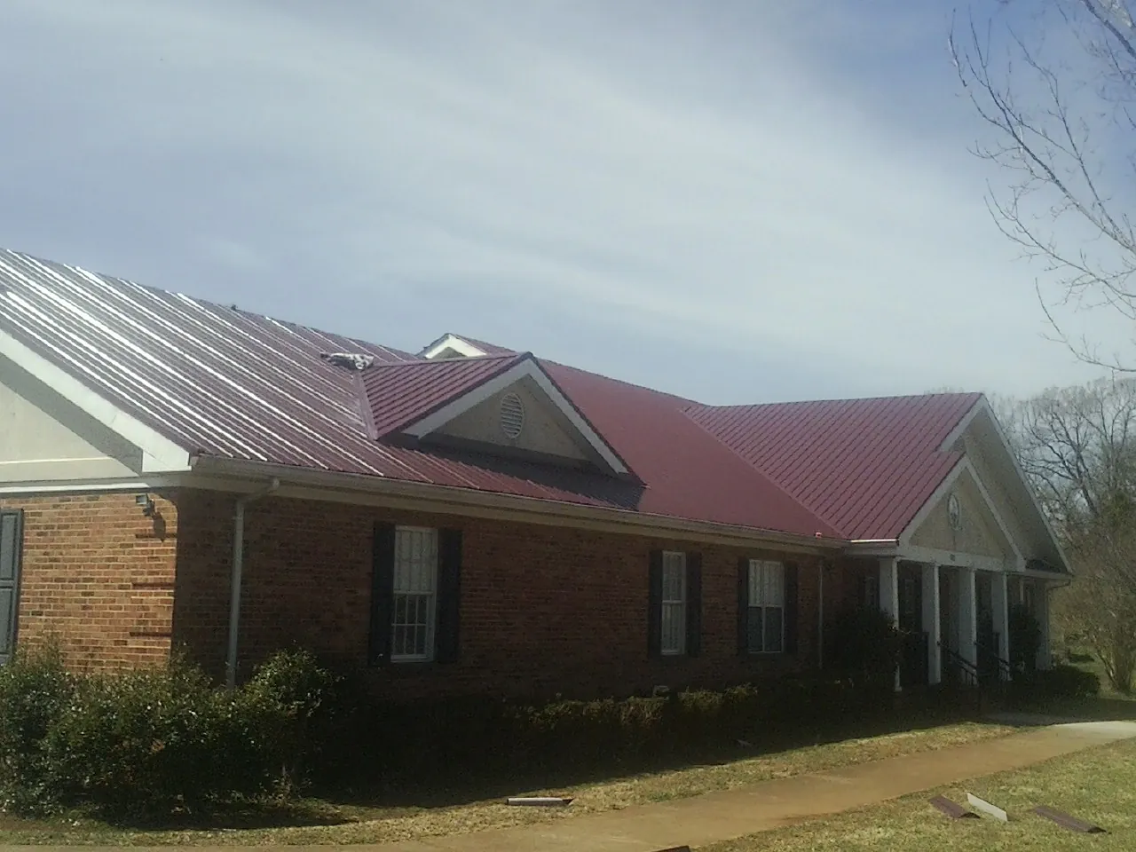 Red metal roof with gabled entries on a long brick building, from a Hail Damage Roof Repair job in Mason