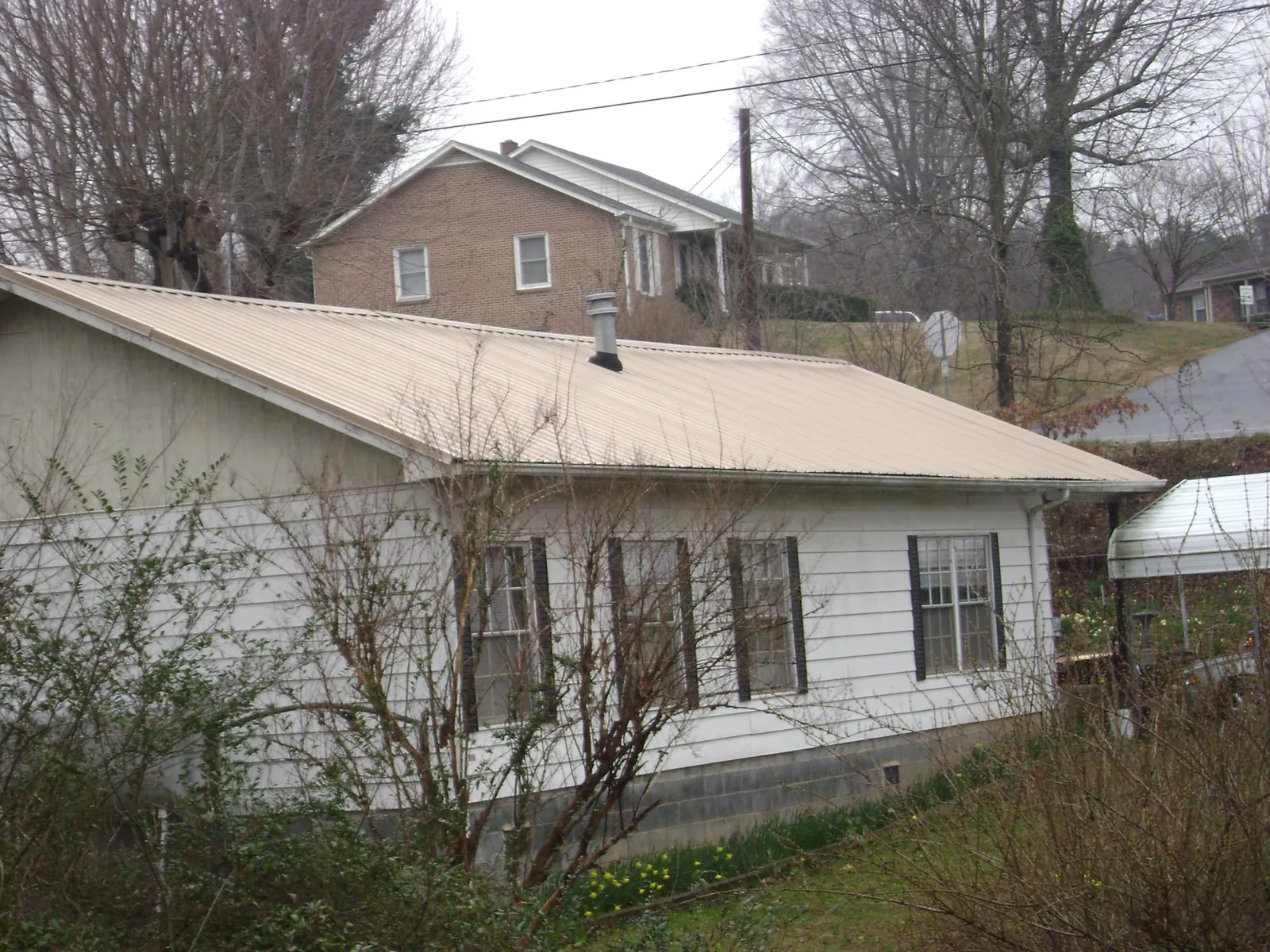 Tan metal roof on a white sided house set into a hillside — Commercial Roofing by Roofing Brothers in Mason
