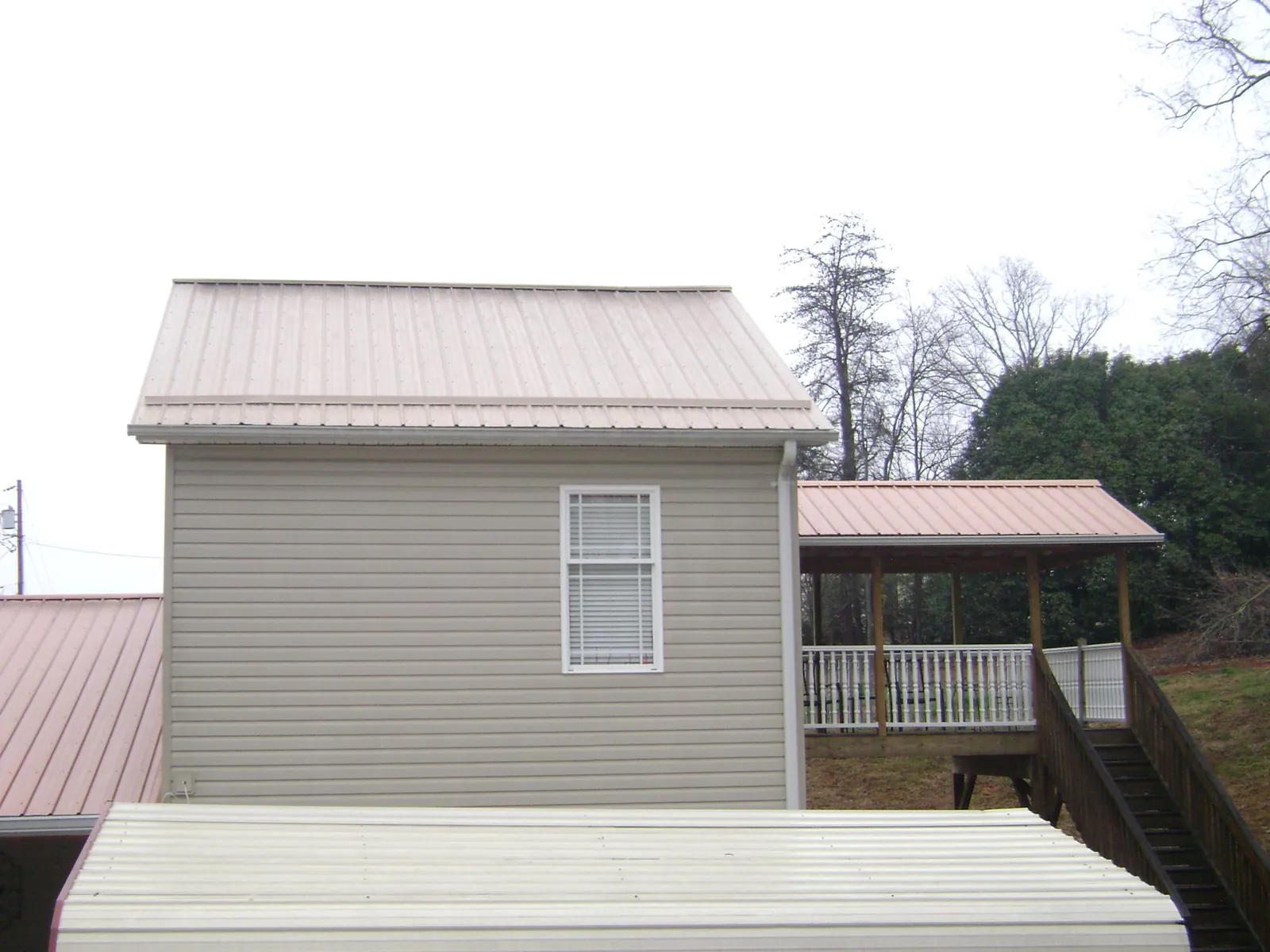 Tan metal roofs on a two story addition and attached porch, from a Roof Replacement job in Mason
